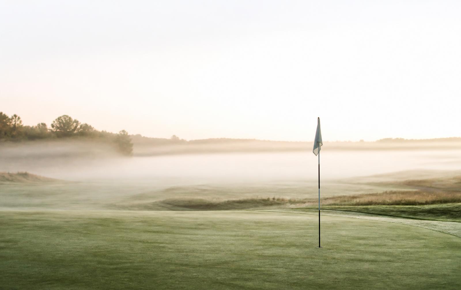 Golfgreen i morgentåke med flaggstang
